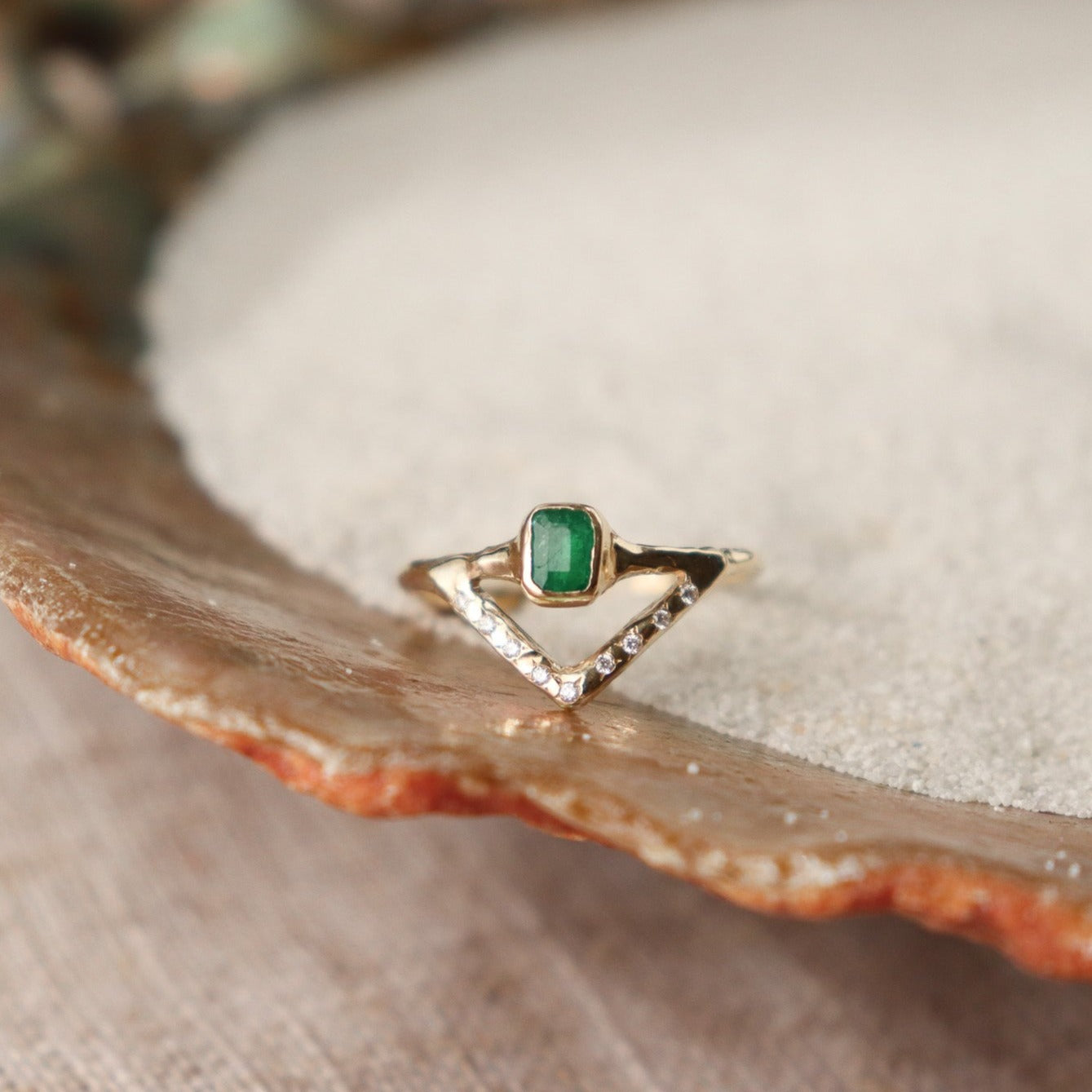 Stunning emerald ring with a bezel-set, rich green gemstone elegantly perched on a delicate, narrow band. Beneath it, a gracefully designed V-band features organically set diamonds, adding a touch of nature-inspired luxury to your jewelry collection.