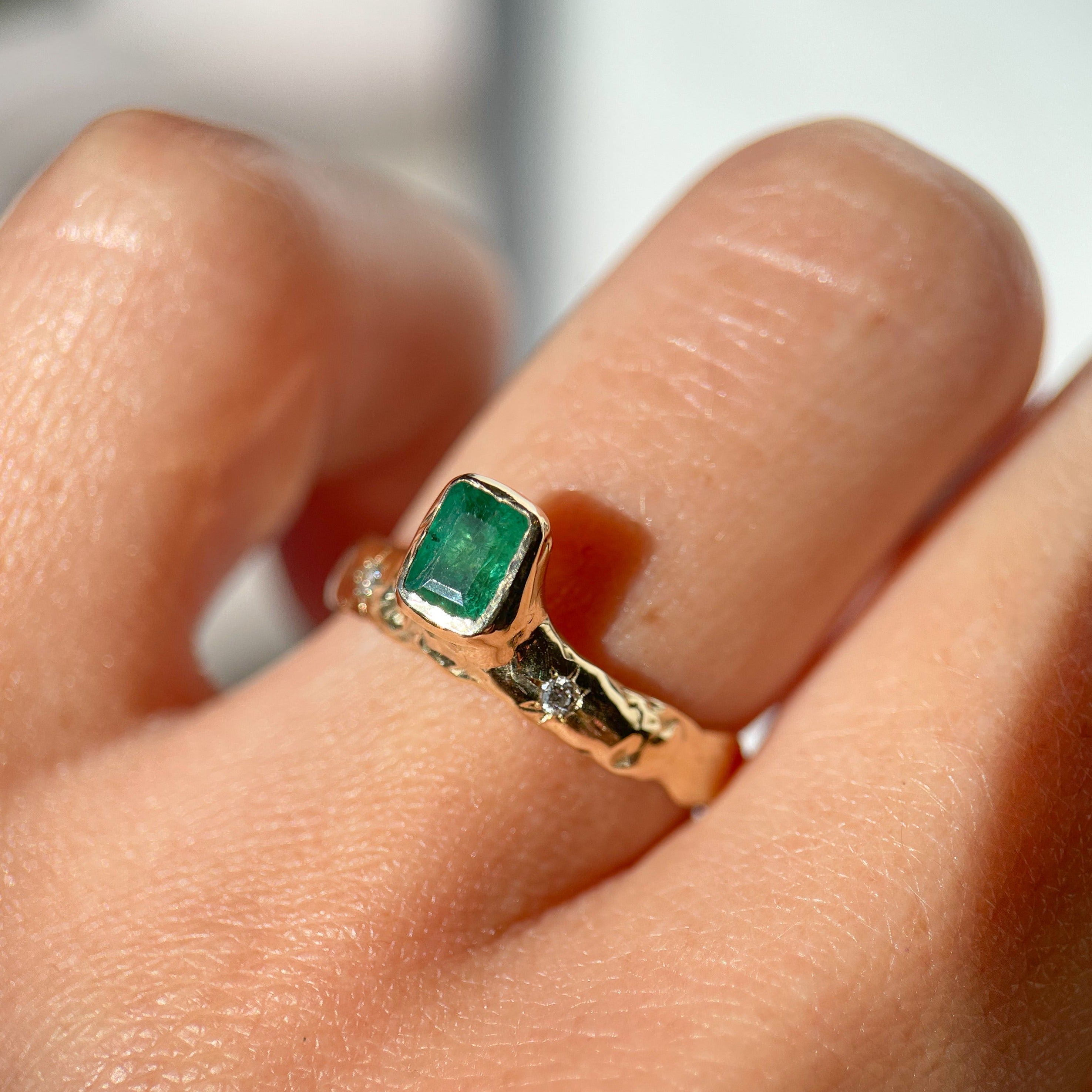An emerald cut  emerald is bezel set in 14k gold  on a wide band with two star set diamonds on the side of the main stone.