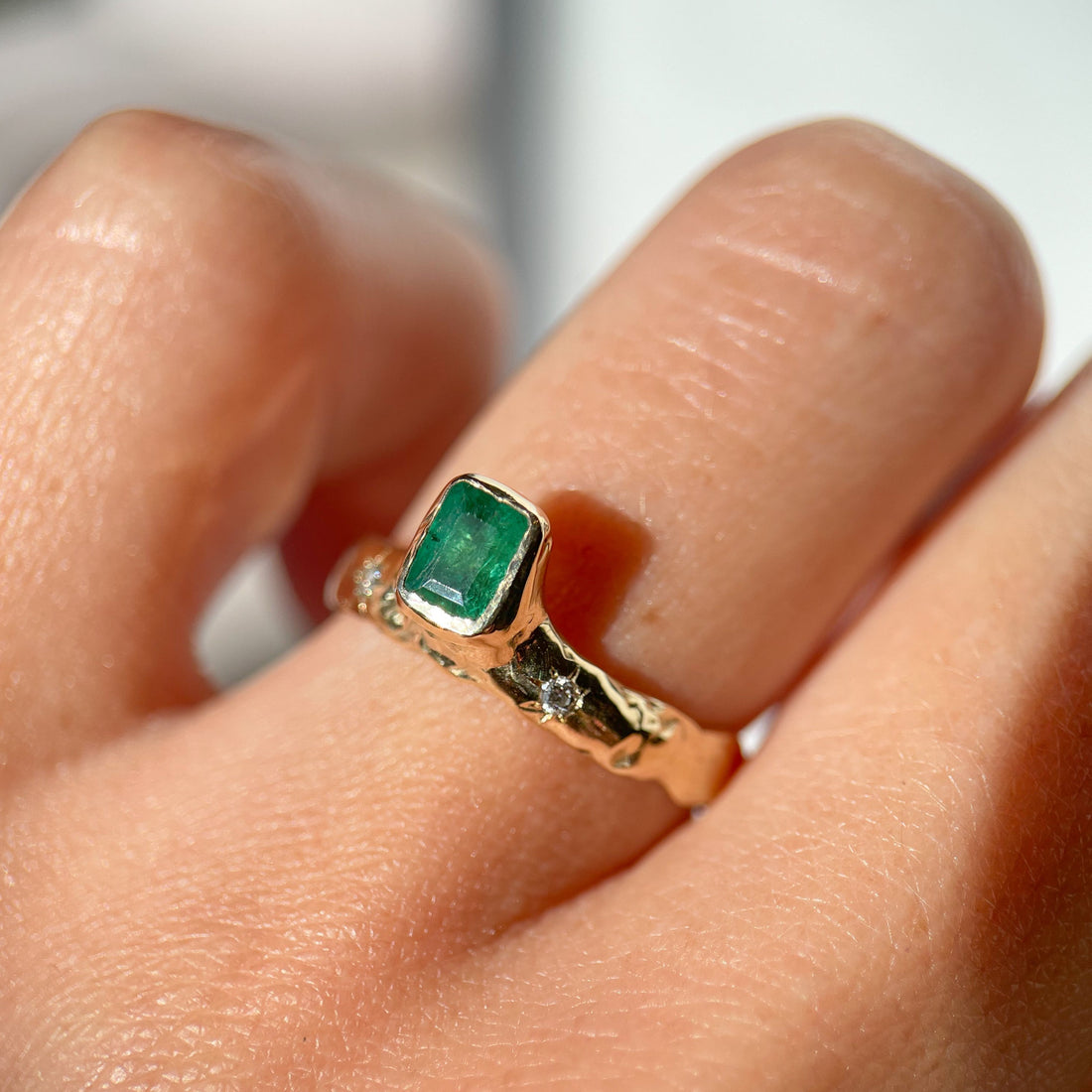 An emerald cut  emerald is bezel set in 14k gold  on a wide band with two star set diamonds on the side of the main stone.