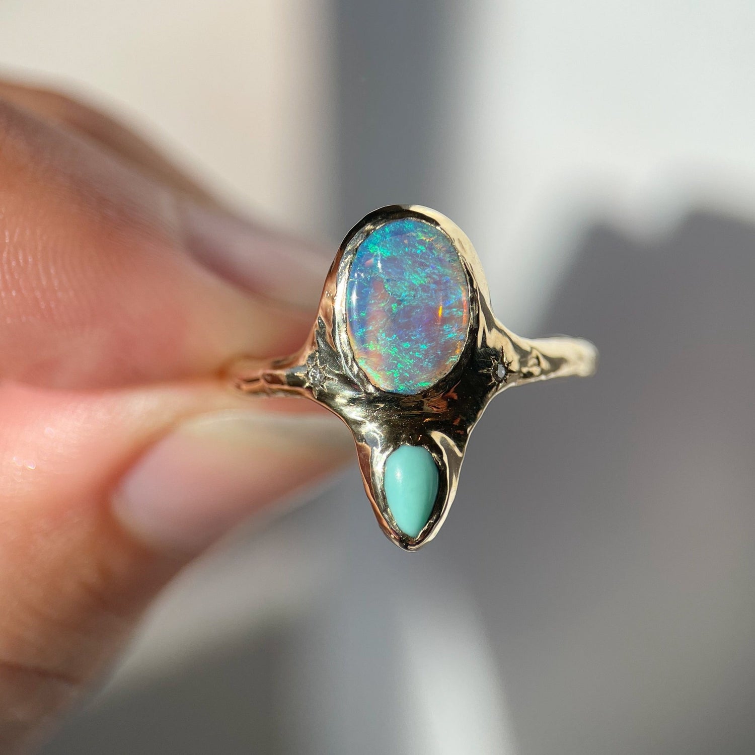 An oval opal is bezel set with a small pear shaped turquoise set underneath it,  this ring has two star set diamonds on each side  of  the center stone.
