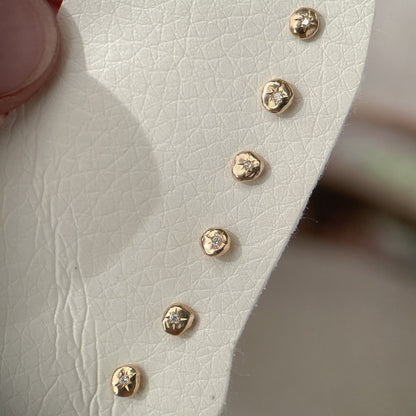 Multiple one of a kind tiny 14k gold circle studs with star set diamonds in the centers.
