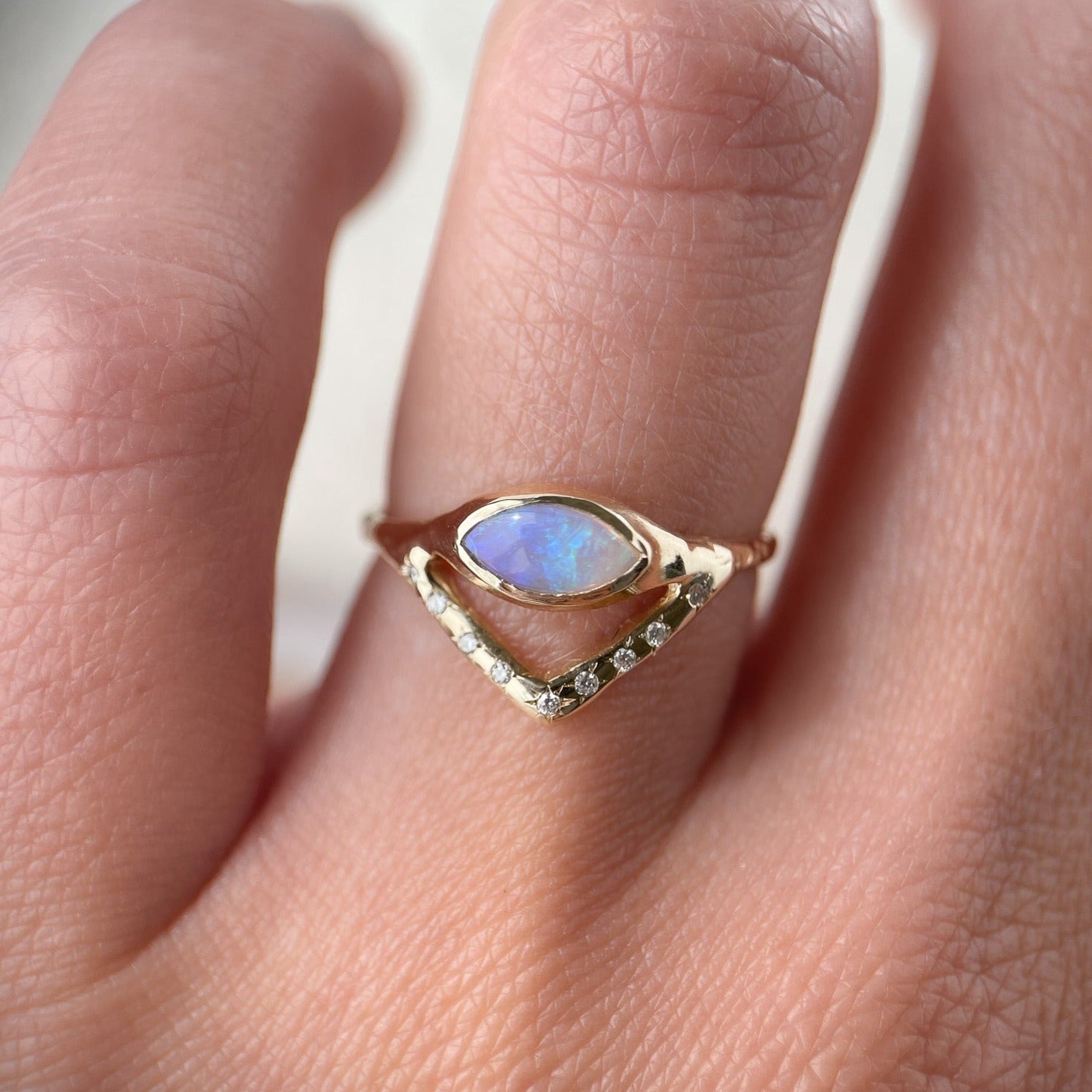 Horizontal marquise opal on a slender band with an organic diamond-set V accent, creating a stunning and unique ring design. Worn to show scale.