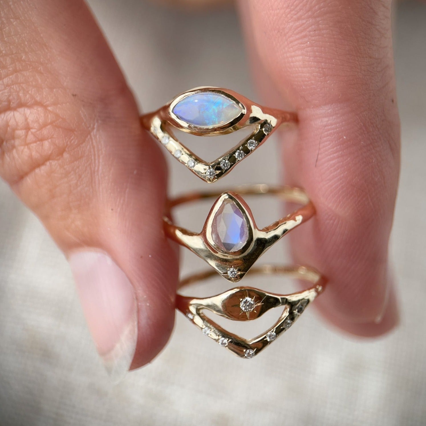 Pear-shaped moonstone, bezel-set with a dazzling diamond star positioned at the base, stacked with an opal ring and a diamond ring.