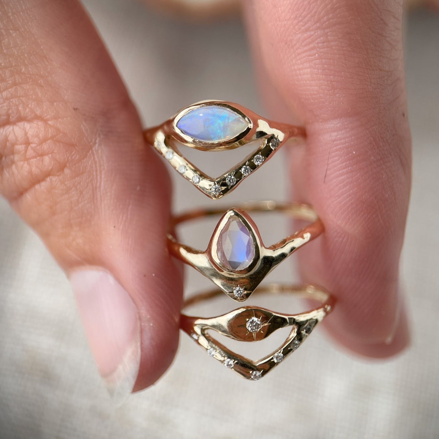 Horizontal marquise opal on a slender band with an organic diamond-set V accent, shown with a pear moonstone ring and an all diamond stacking  ring.