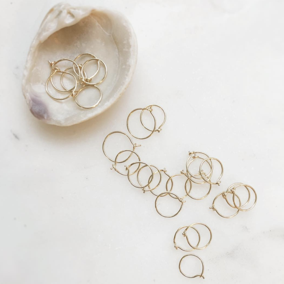 Small gold hoop earrings are scarred about next to a seashell