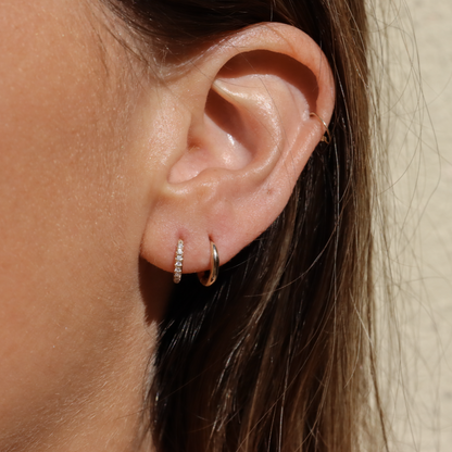An ear with the classic and diamond pave hinge huggie hoops to show size