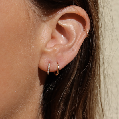 A pave diamond gold hoop and a plain hoop are worn in an earlobe to show the comparison 