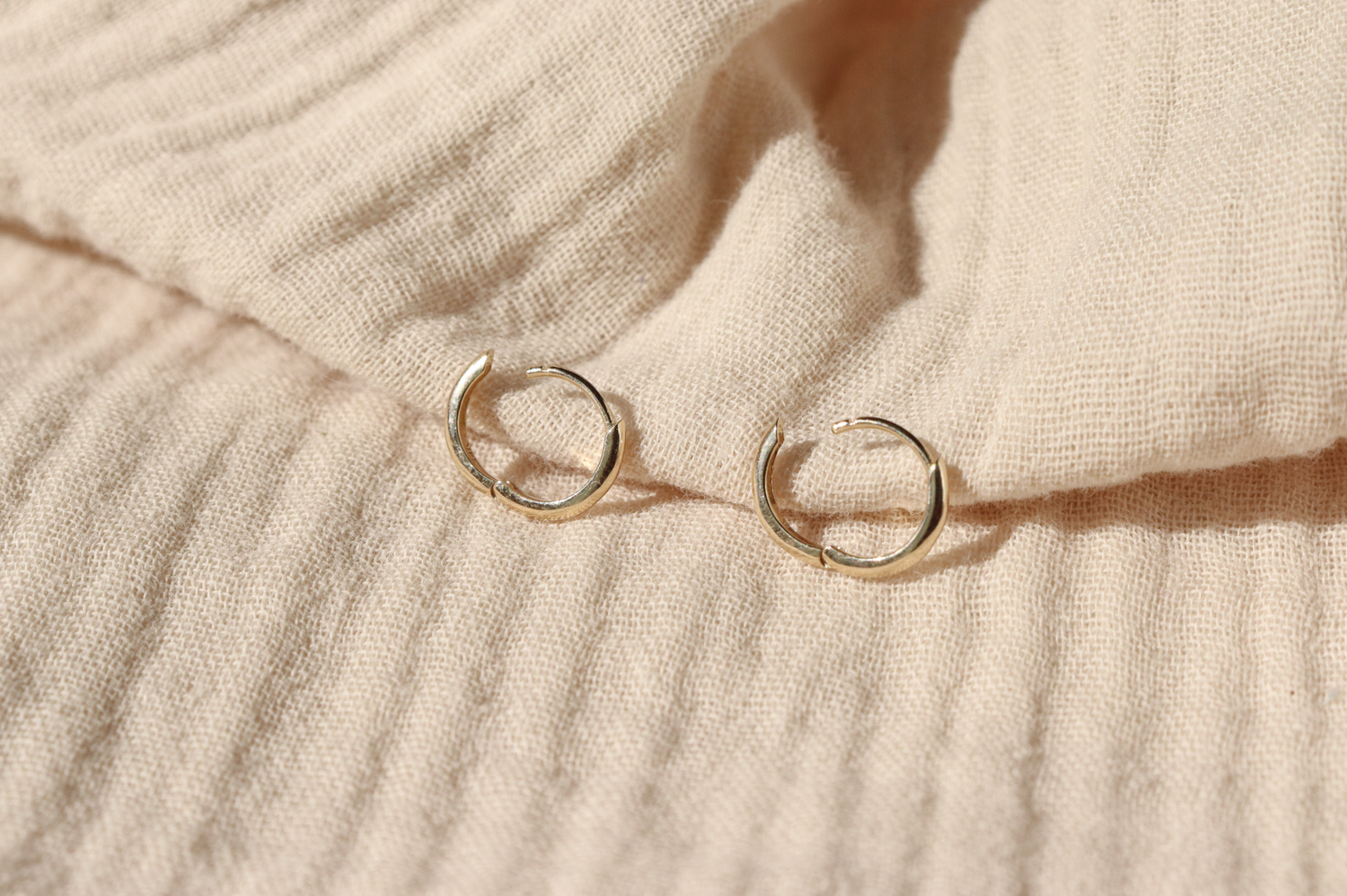 A pair of classic 14k gold hinge huggie hoops are laid out open to show how the hinge works