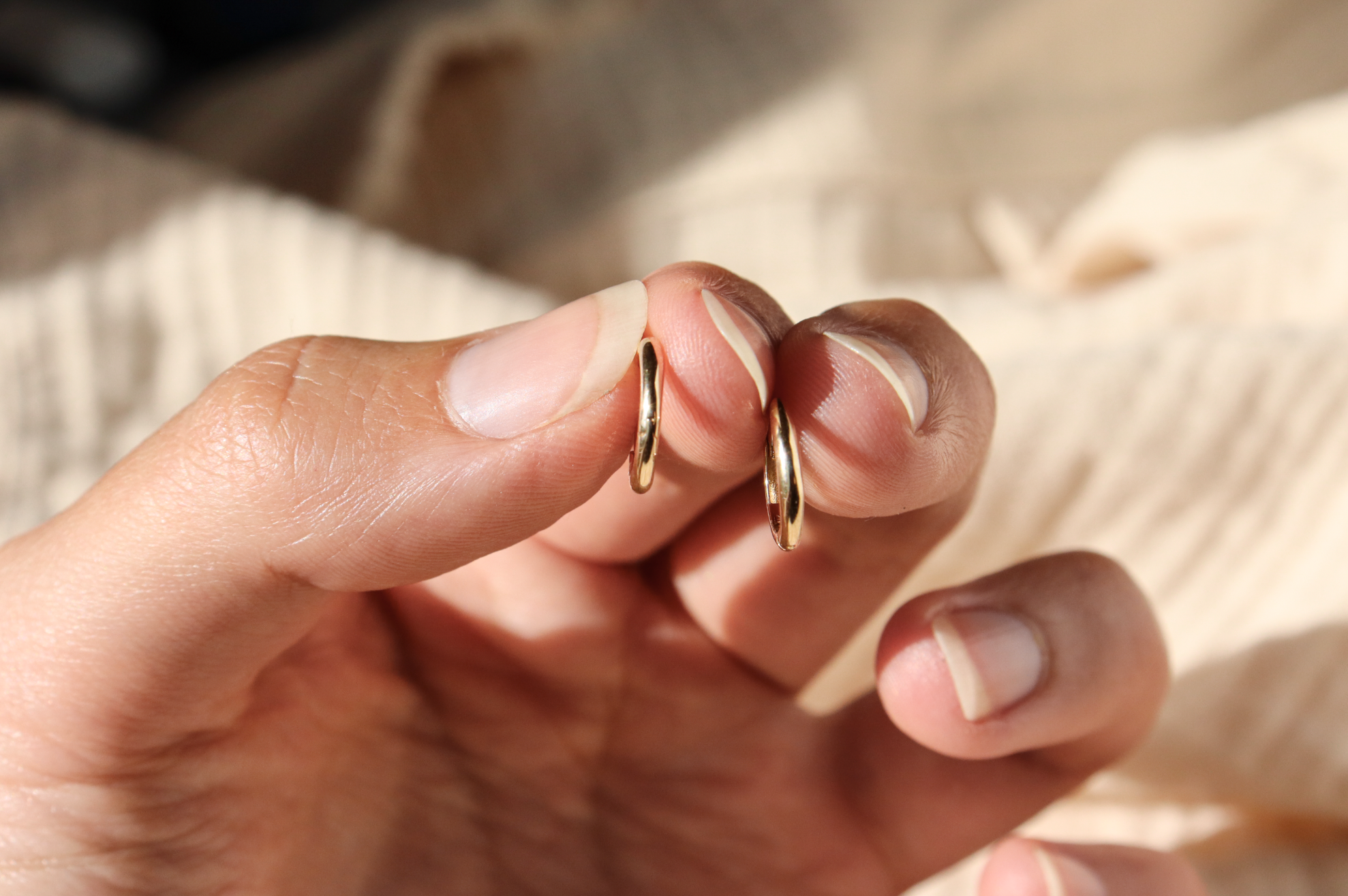 Hand holding a pair of classic 14k gold hinge huggie hoops