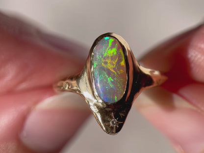 Close up video of a long oval opal that is bezel set in 14k gold  with  a star set  diamond at the base of the ring.