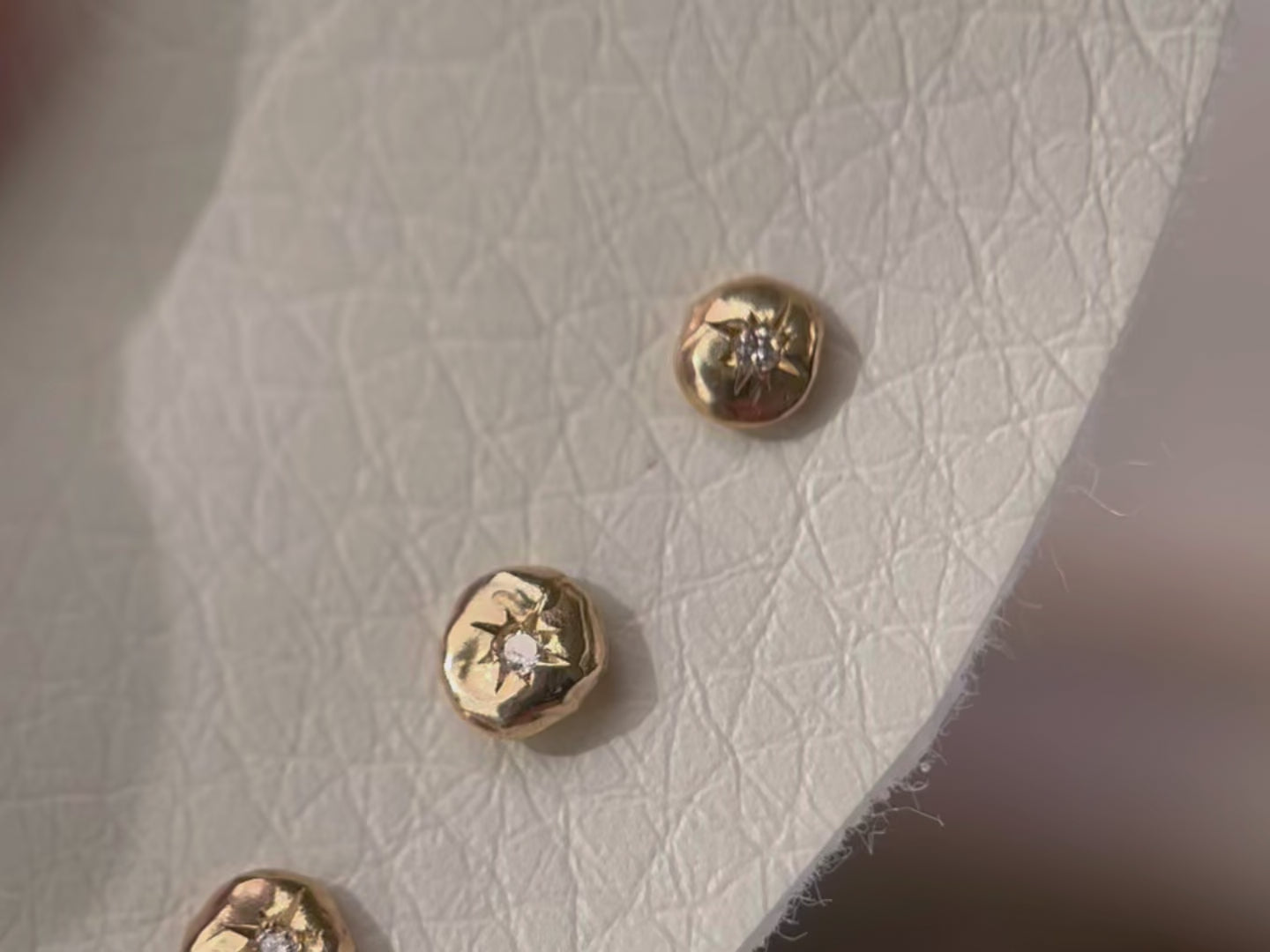 A close up video of multiple one of a kind tiny 14k gold circle studs with star set diamonds in the centers.