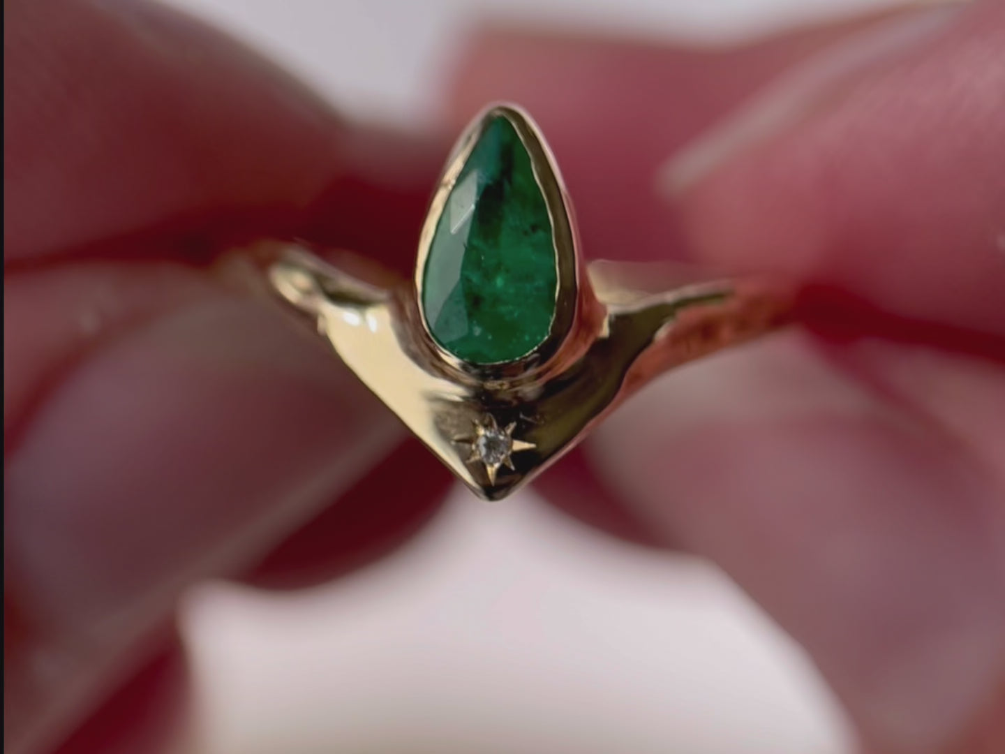 A close up video of a pear-shaped emerald bezel-set with a brilliant diamond star at its base, creating a striking and celestial-inspired jewelry piece.