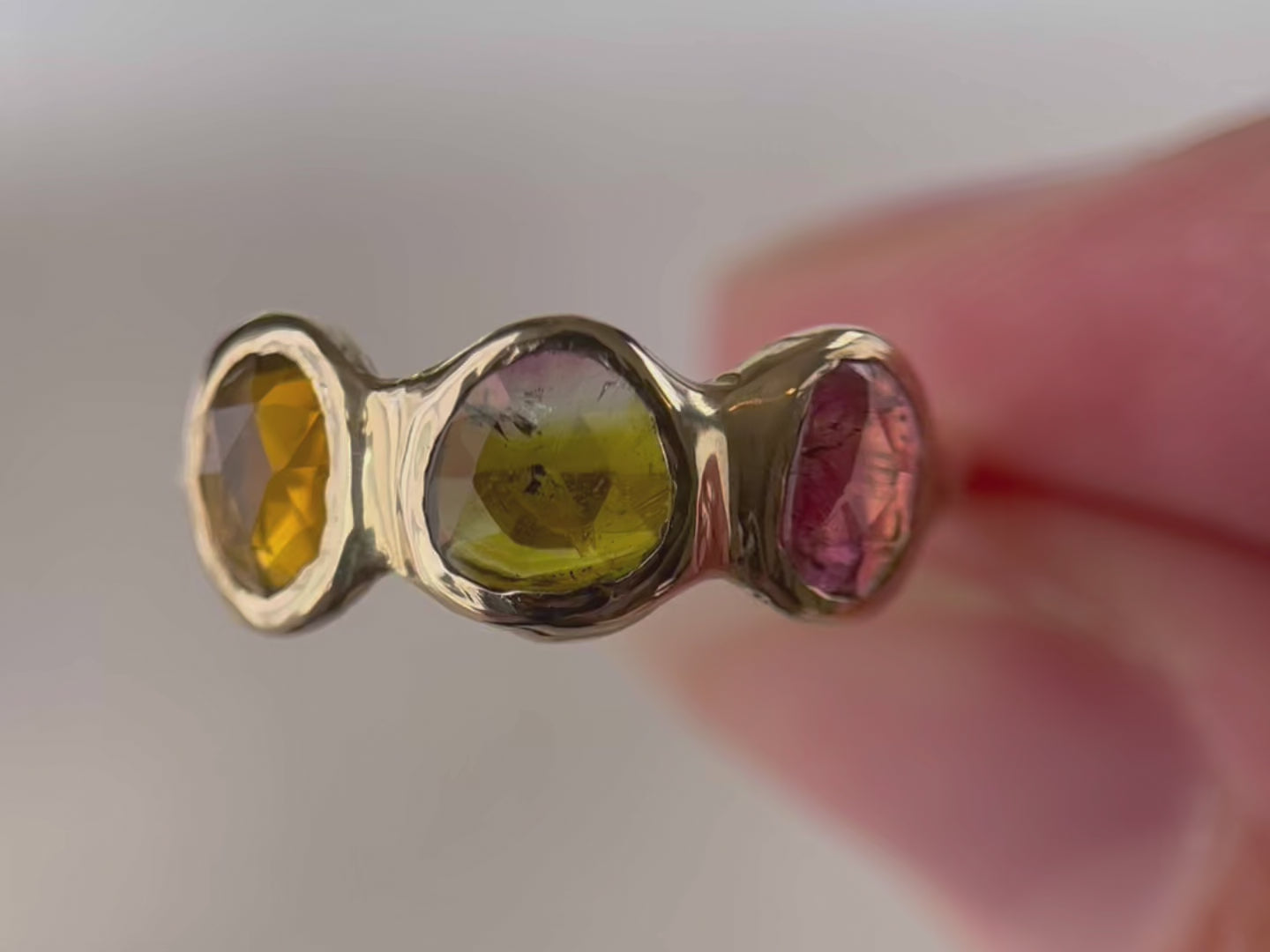 A close up video of watermelon tourmaline gemstones that are bezel set along the front of a 14k gold band.