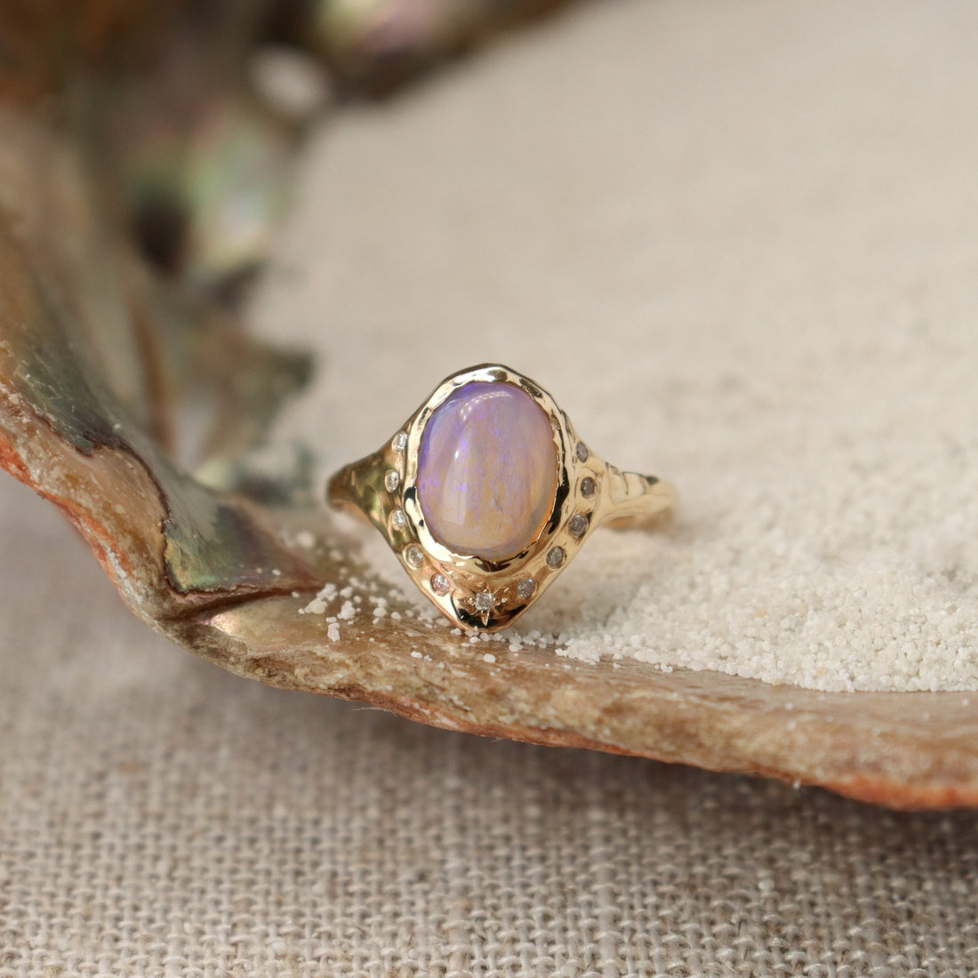 An oval opal is  bezel set in 14k gold with diamonds  set all around it,  there is a star set diamond at the base, and the band is organically crafted..