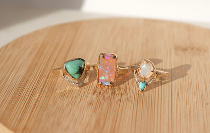 three gemstone rings are displayed side by side on a wood background